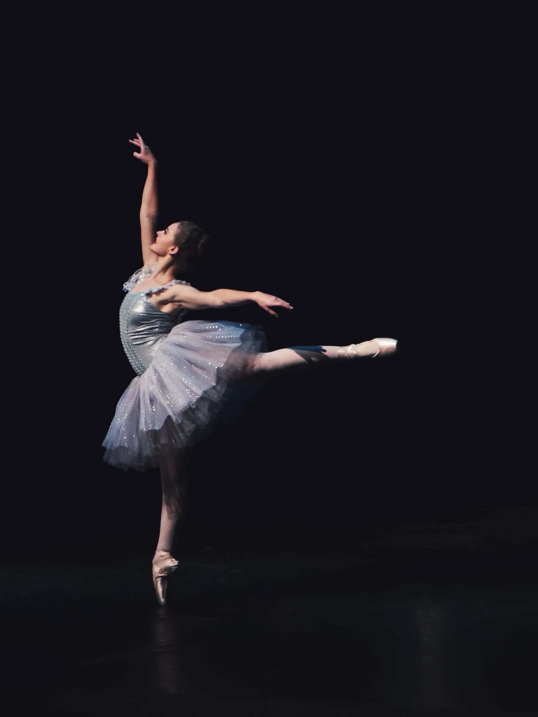 Malena Ríos en arabesque sobre puntas, tutú clásico, fondo oscuro